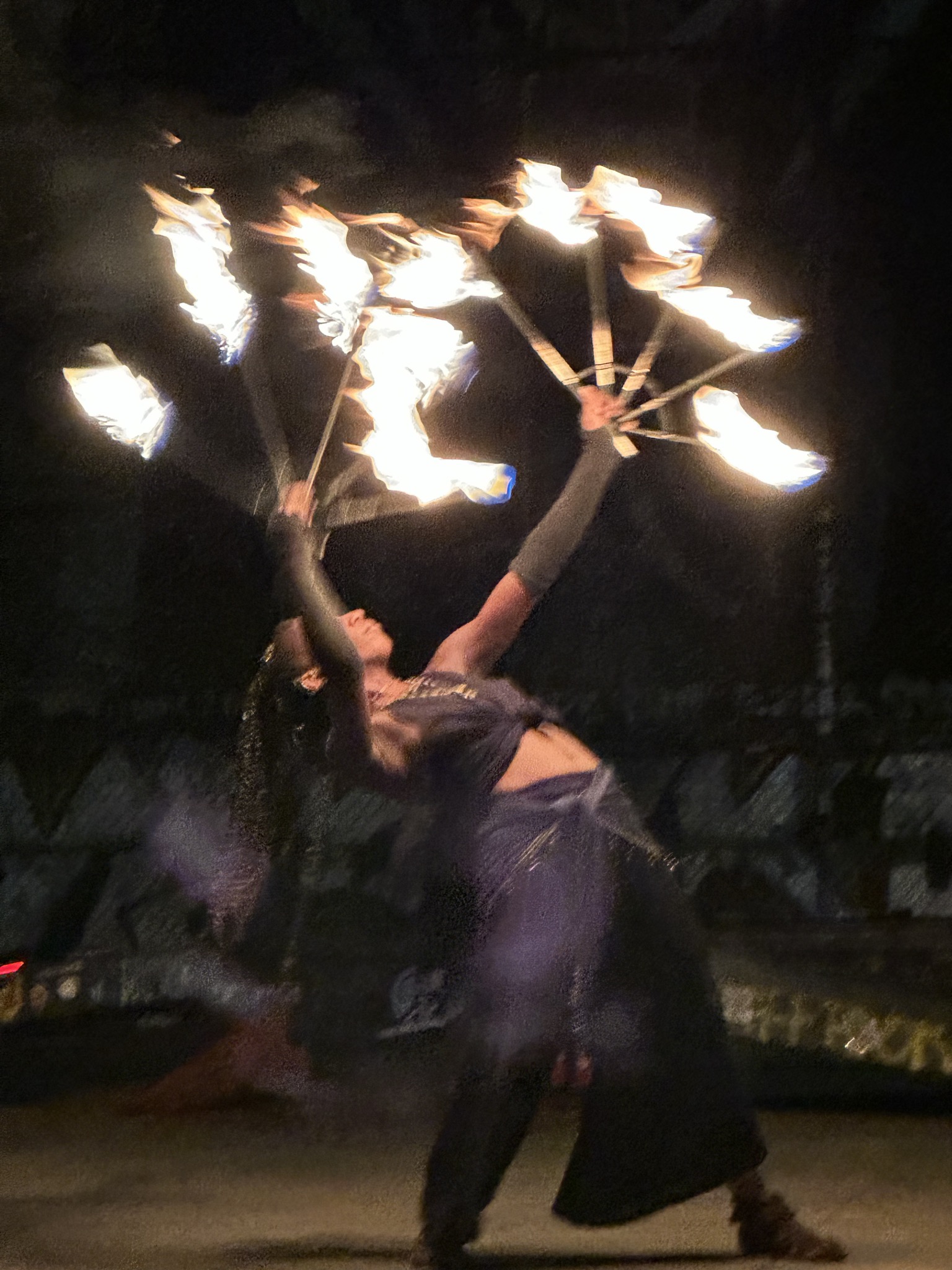 A fire dancer at night, two fans of flame blurred mid-spin