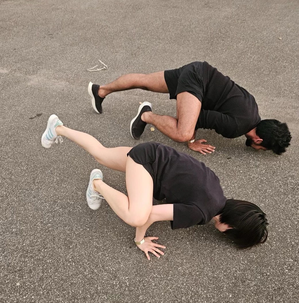 Two people in matching black folded face-down on the asphalt, sneakers in the air